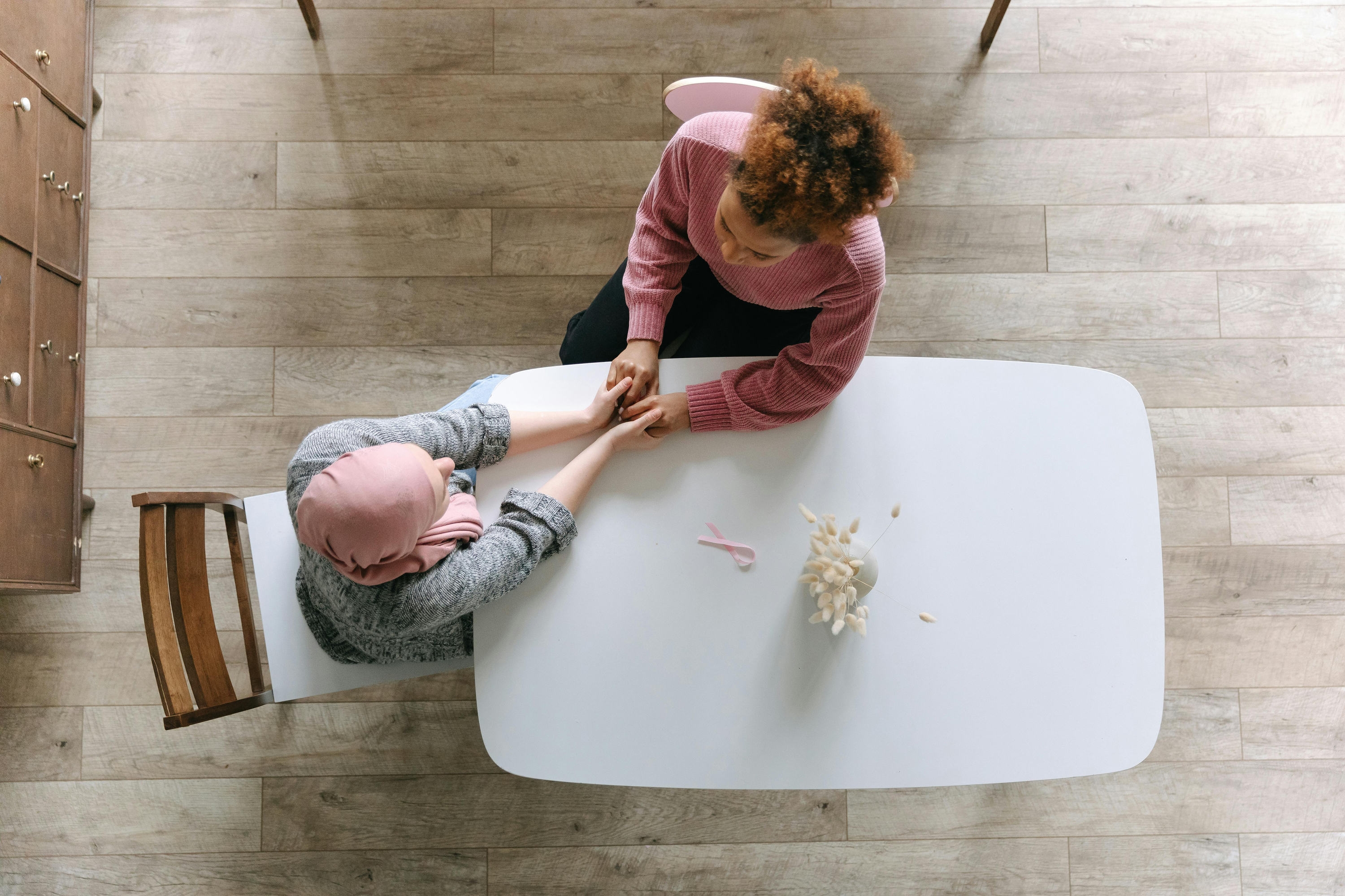 Two women sitting at table holding hands